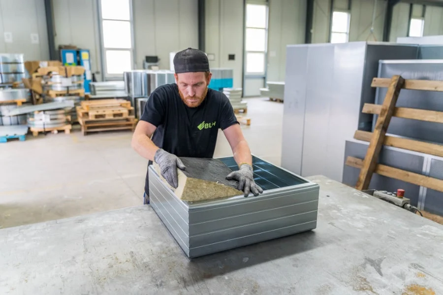 Mitarbeiter der BLH füllt einen Kulissenrahmen mit Mineralwolle